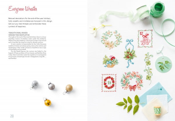An open book, The Magic of Christmas to Cross Stitch by Schiffer Publishing, Ltd., shows holiday wreath and mistletoe text on the left page; the right displays Christmas cross-stitch patterns with ribbons, greenery, ornaments, and fabric on white.