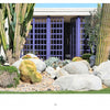 Showcasing the Palm Springs Mid-century Modern style by Schiffer Publishing, Ltd., a modern building with purple grid doors is set among large cacti, agave, rocks, a desert landscape, and green grass in the foreground.
