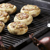Stuffed mushrooms with a browned filling are grilled to perfection on a ridged pan, ideal for trying new recipes from Pure BBQ! by Schiffer Publishing, Ltd. Whole red onions sit in the foreground on a dark surface.