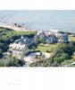 An aerial view from "United by Design" by Schiffer Publishing, Ltd. shows two large gray-shingled Cape Cod homes, set among greenery and landscaped lawns, with a driveway and shoreline waves in the background.