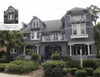 A large gray shingle-style house with white trim, featured in "Florida's Historic Victorian Homes" by Schiffer Publishing, Ltd., showcases multiple gables, balconies, palm trees, a covered front porch, and detailed upper shingles.