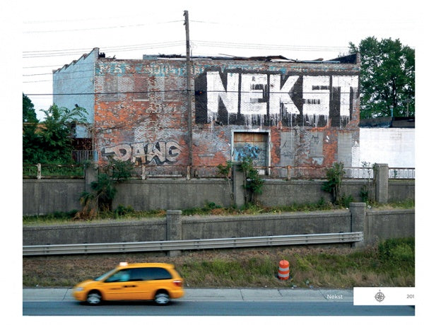 A yellow taxi passes a weathered brick building featuring Detroit Graffiti by Schiffer Publishing, Ltd.—large white NEKST and smaller gray PHANG—while overgrown plants line the concrete barrier, enhancing the street art scene.