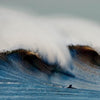 Two surfers watch a powerful Atlantic wave crest under a clear sky, embodying the thrill of surf culture as featured in "Surf NYC" by Schiffer Publishing, Ltd.