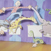 A green modeling-clay character reacts in surprise to five playful cutouts on a blue-purple wall under the text “Zuh-oh!”—capturing the whimsy of Gruel Snarl Draws a Wild Zugthing from Schiffer Publishing, Ltd.